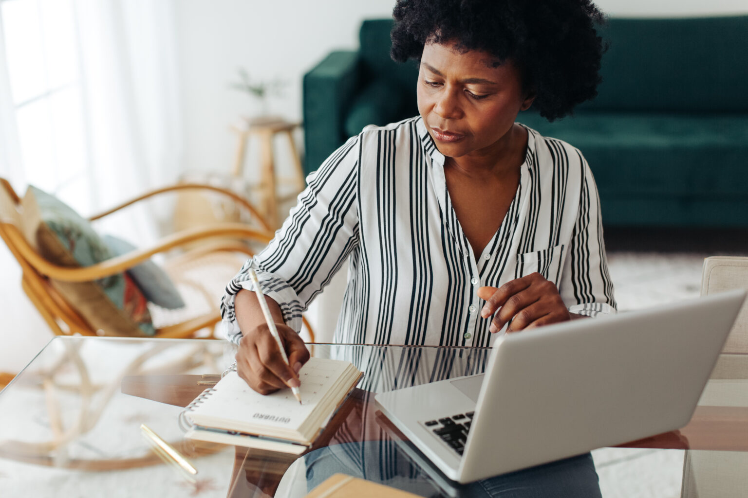 Woman sitting at table and taking notes in front of laptop