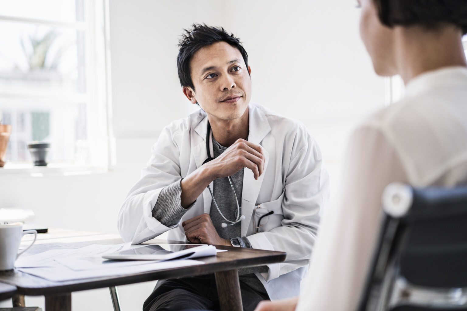 A photo of doctor discussing with patient at table. Woman consulting to male expert. They are sitting in hospital.