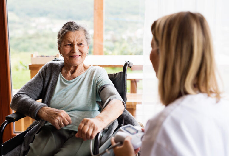 A nurse checking blood pressure of a woman in a wheelchair.