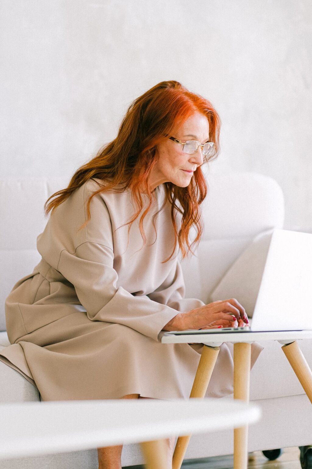 late-middle aged woman sitting on couch, scrolling on laptop