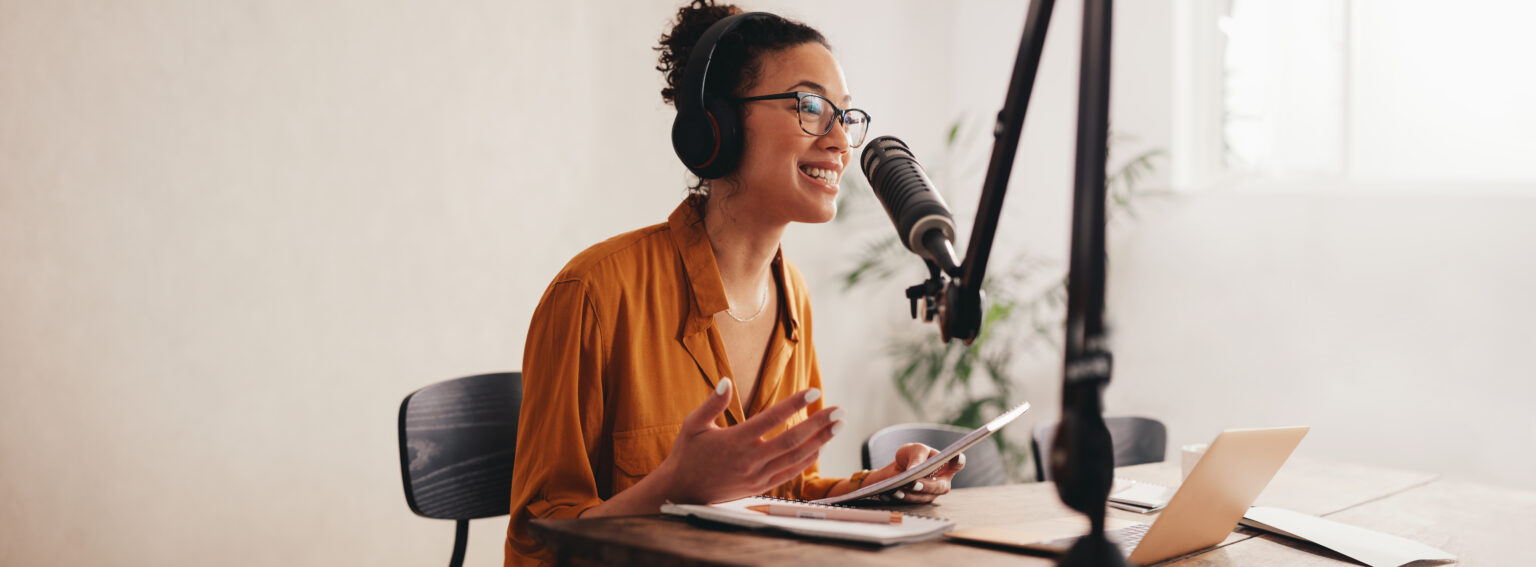 Woman recording a podcast on her laptop computer with headphones and a microphone.