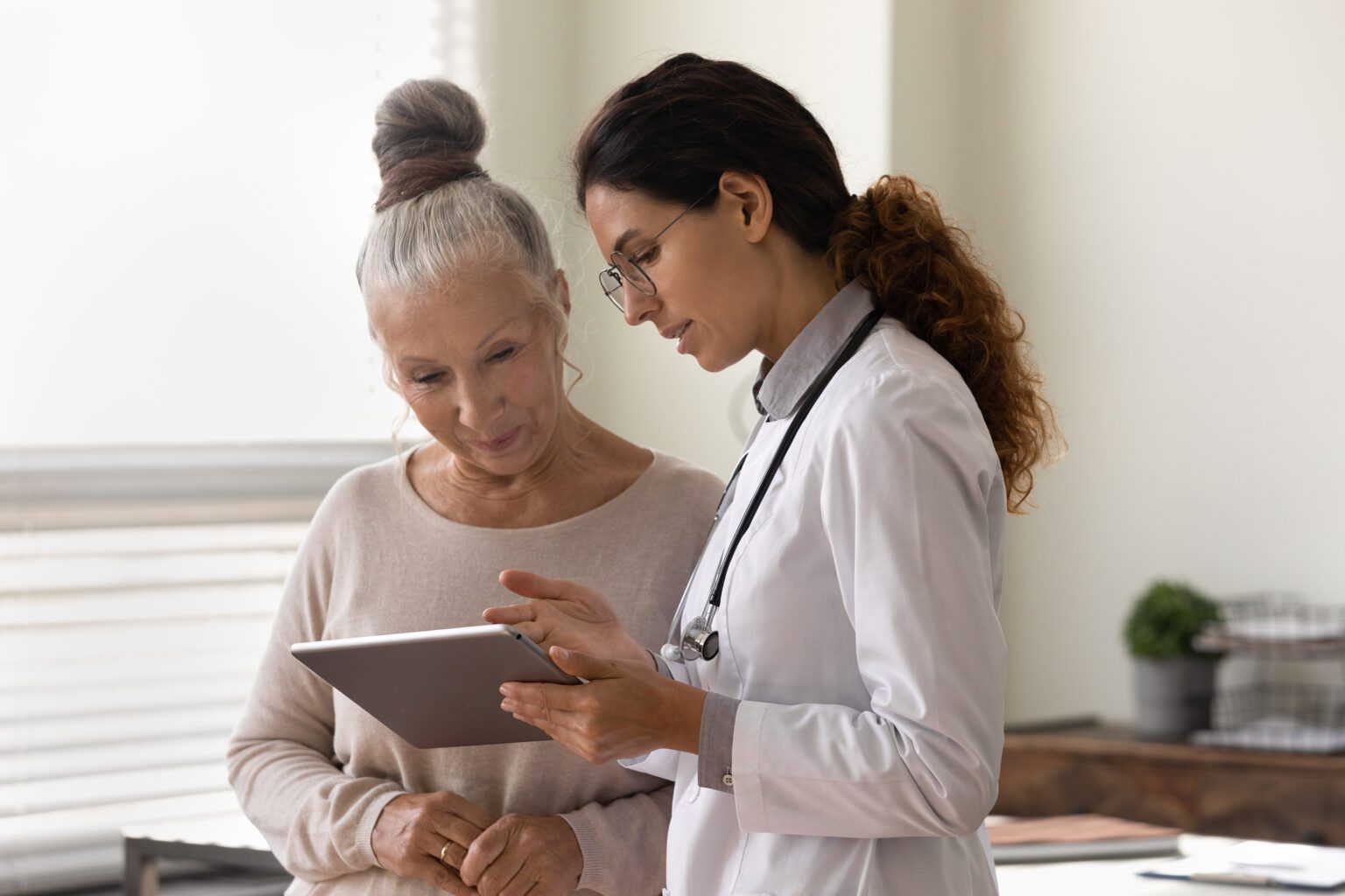 Serious GP doctor showing tablet screen to old 70s female patient, explaining electronic prescription, medical screening, examination result, giving consultation.