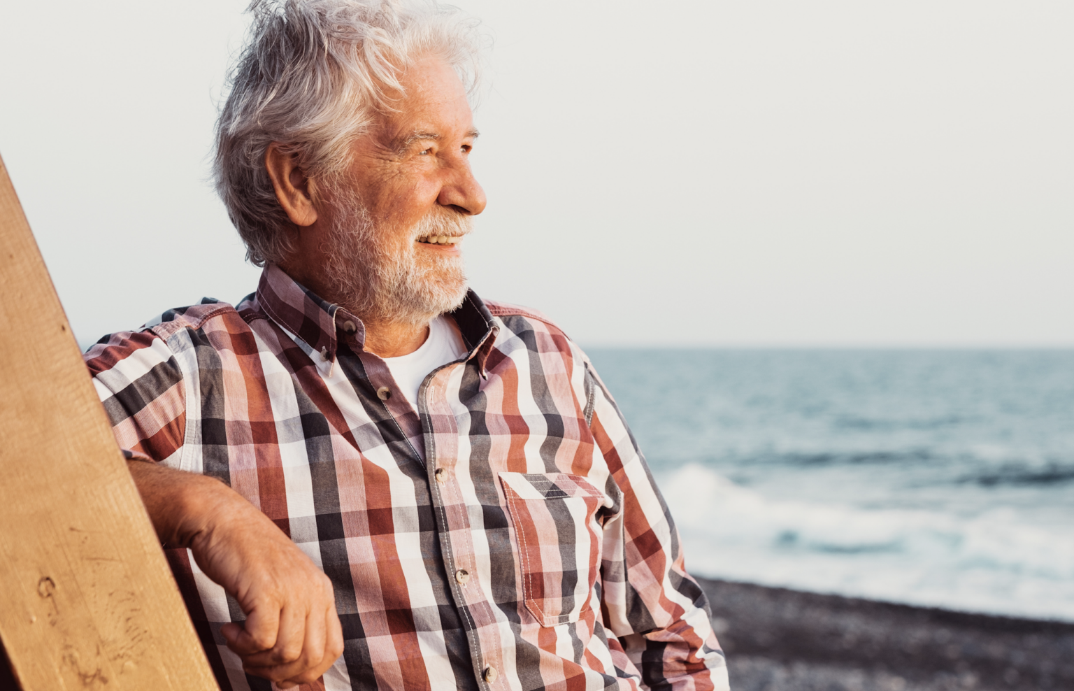 A man with gray hair and an orange checkered shirt looking out across the water.