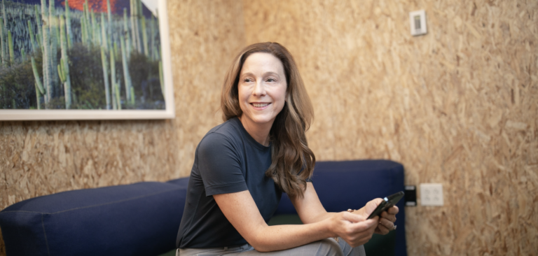 Suzanne sitting on a blue couch holding a cell phone.