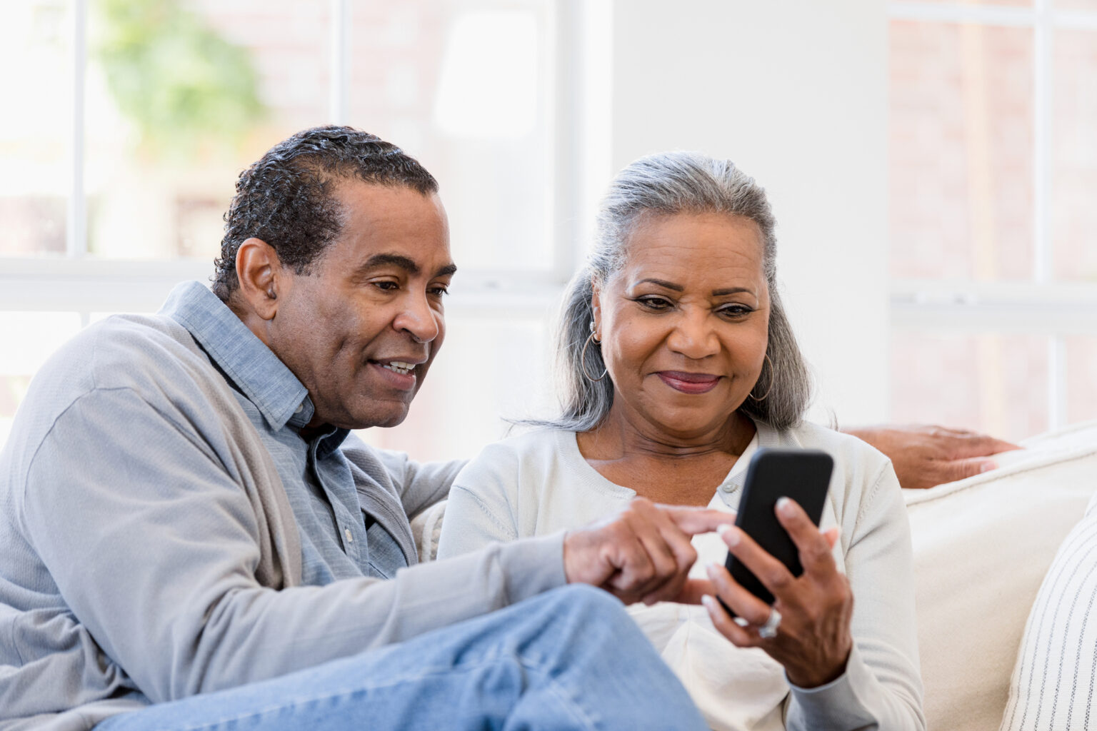 The husband and wife sit on the couch and read an article on their phone.