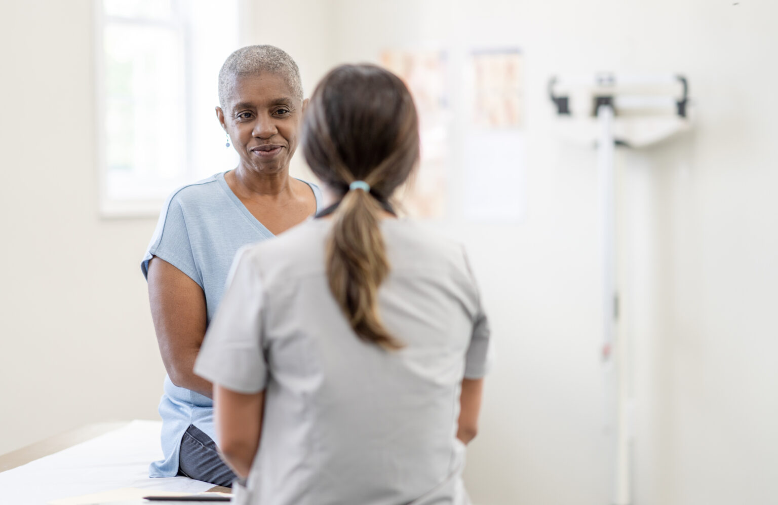 A middle-aged Black woman sits on exam table talking with her doctor.